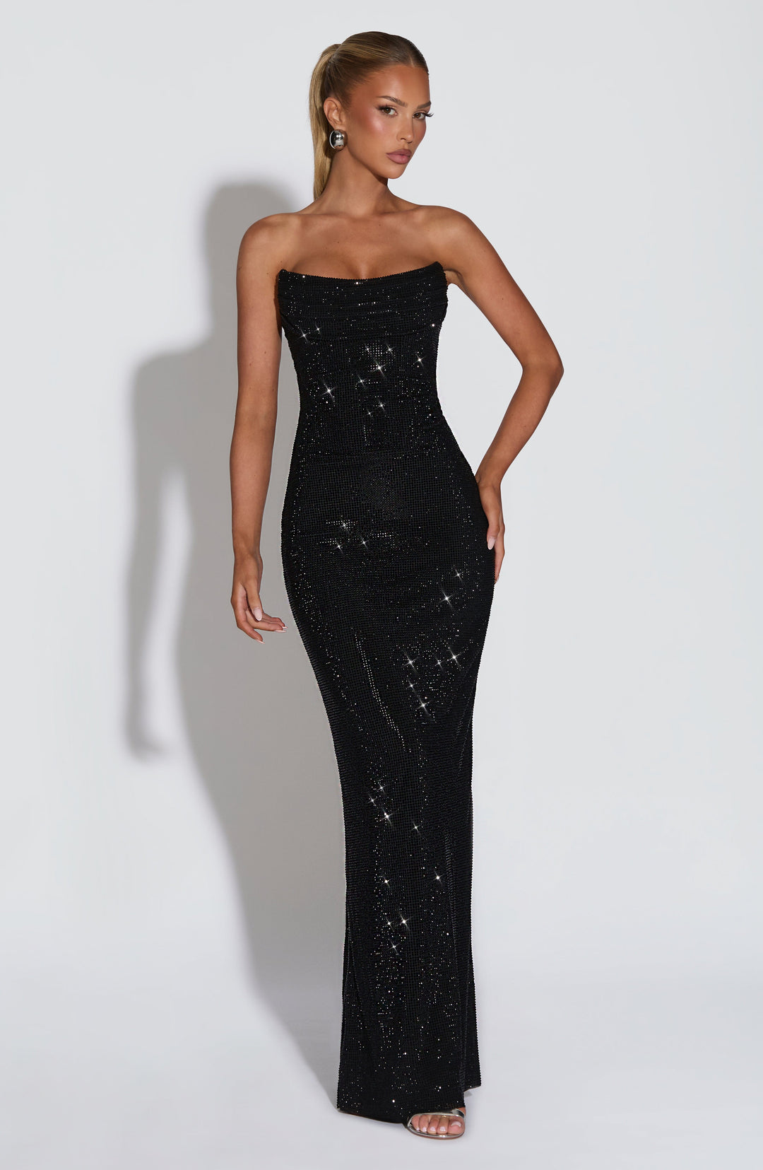 Model wearing the black strapless rhinestone maxi dress, front view, with one hand on her hip 22