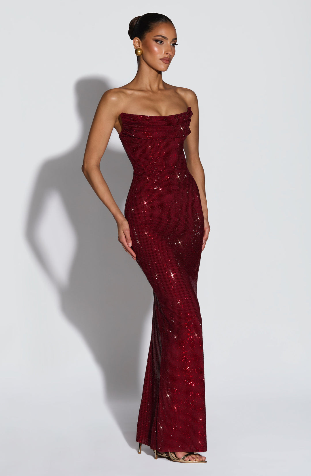 Three-quarter view of the burgundy rhinestone gown worn with gold heels, showing its fitted column shape 4