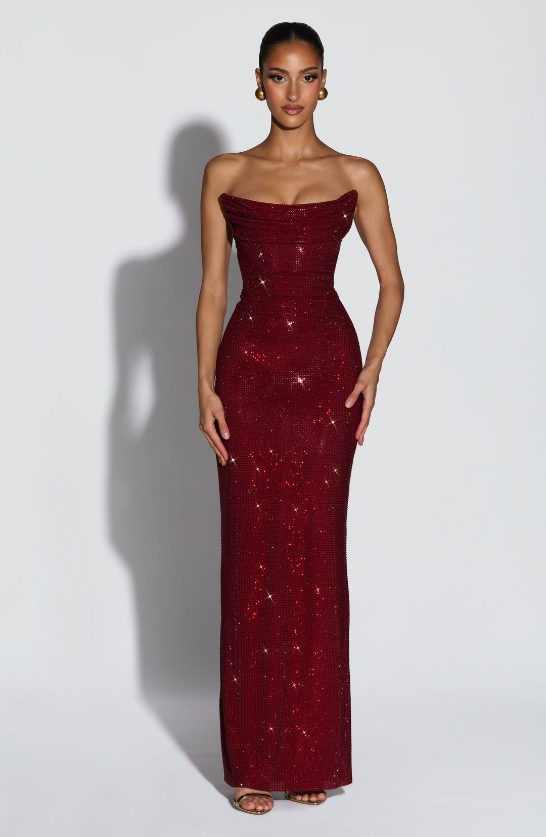 Model faces the camera in the burgundy rhinestone maxi dress with a draped strapless neckline and fitted bodice 1