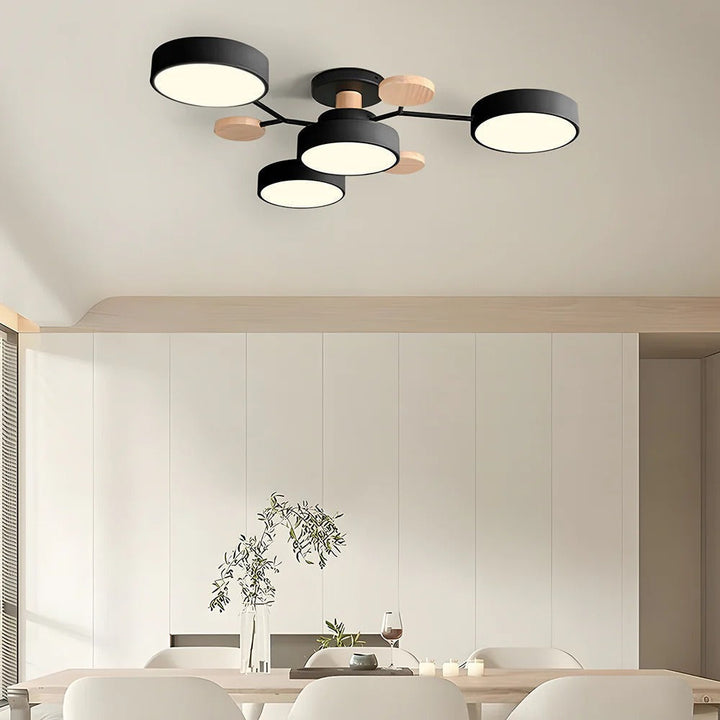 Black four-drum ceiling light with wood discs above a dining table with white chairs and a vase of greenery. 25