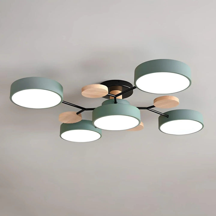 Close view of the ceiling light with five round green drum shades, black branching arms and small wooden discs, all lit. 41