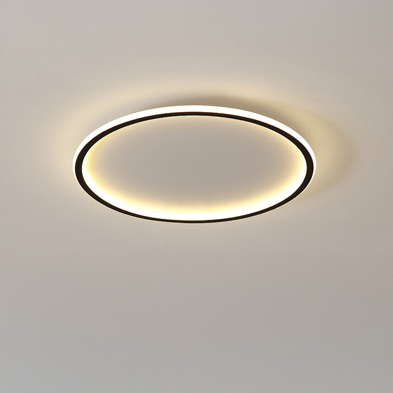 Close-up of the black ring ceiling light turned on, warm light spilling softly across a plain beige ceiling.