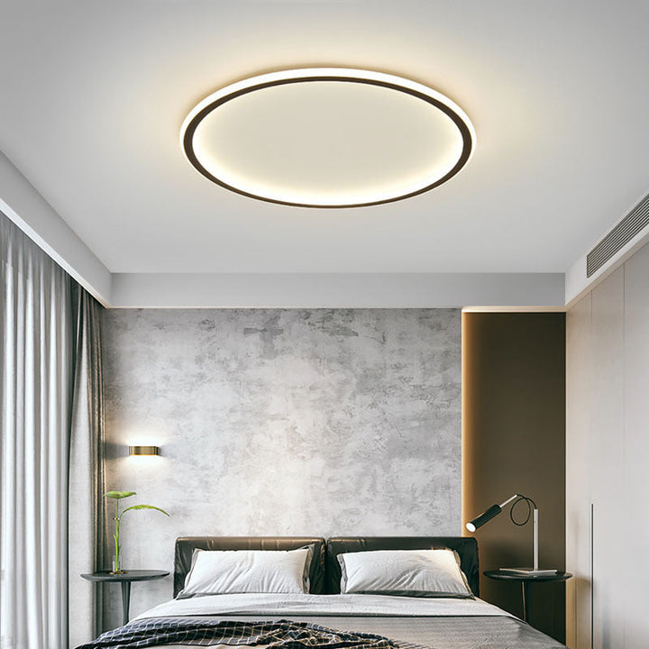 Black ring ceiling light another view above a bed with a concrete-look gray accent wall and a reading lamp.