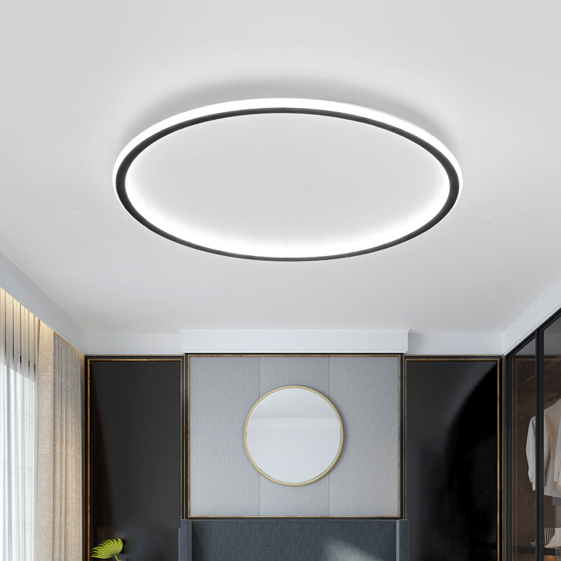 Black ring ceiling light another view shining cool white in a bedroom with a round gold-framed mirror above the headboard.