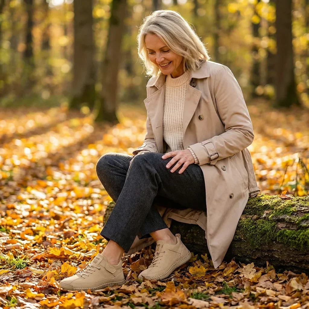 Smiling woman sits on a mossy log in an autumn forest, looking down at her beige sneakers. 13
