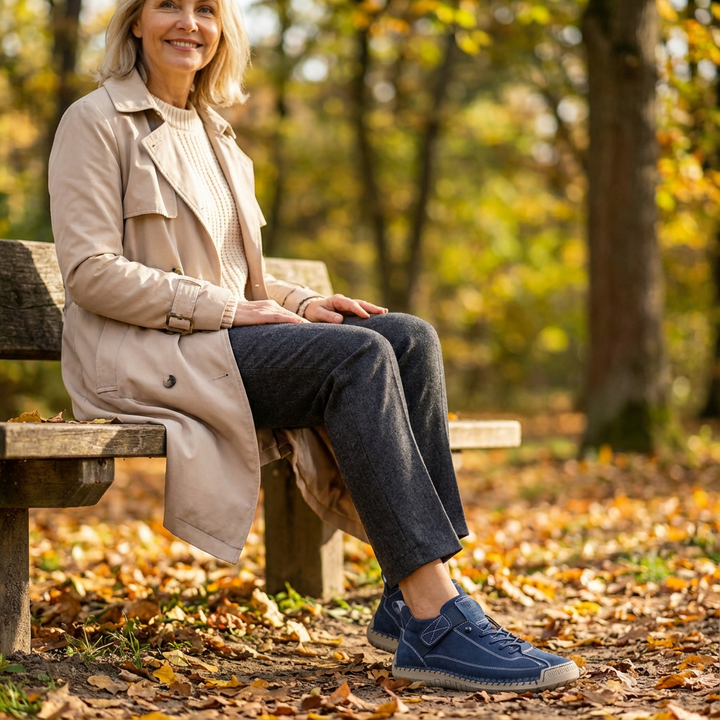 Smiling woman in a beige trench coat sits on a park bench wearing blue sneakers 21