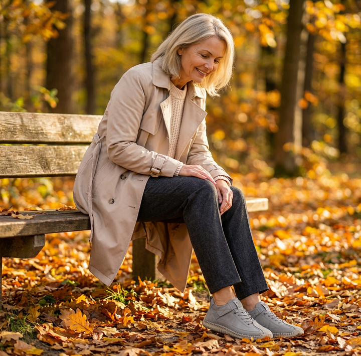 Woman on an autumn park bench looks down at her gray sneakers with strap detail 22