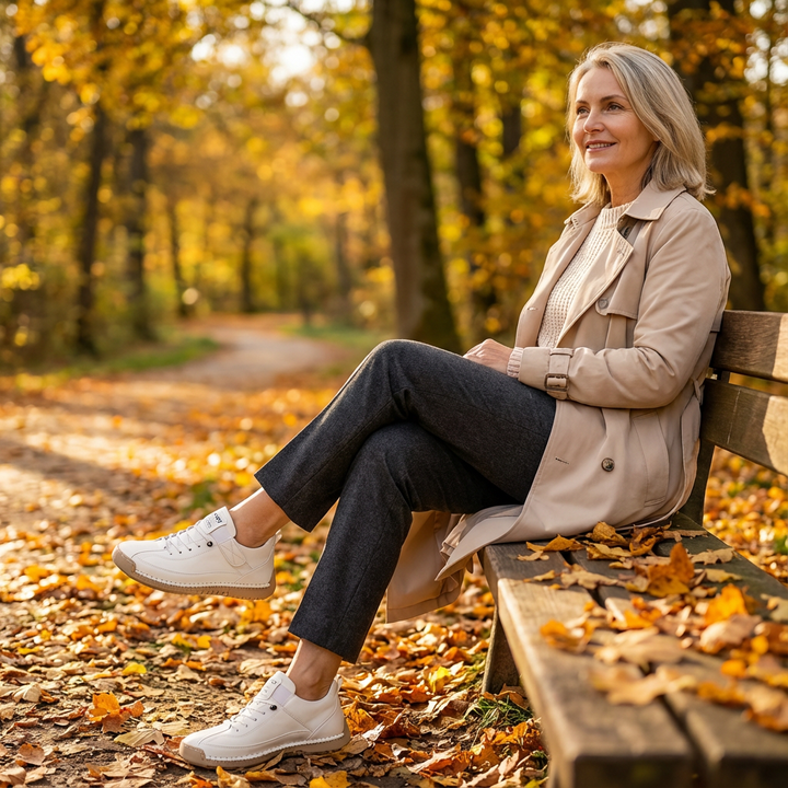 Woman in a trench coat sits on a park bench in autumn wearing white sneakers 16
