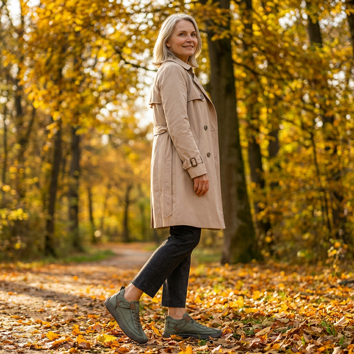 Woman in a trench coat strides down an autumn forest path wearing green sneakers 19