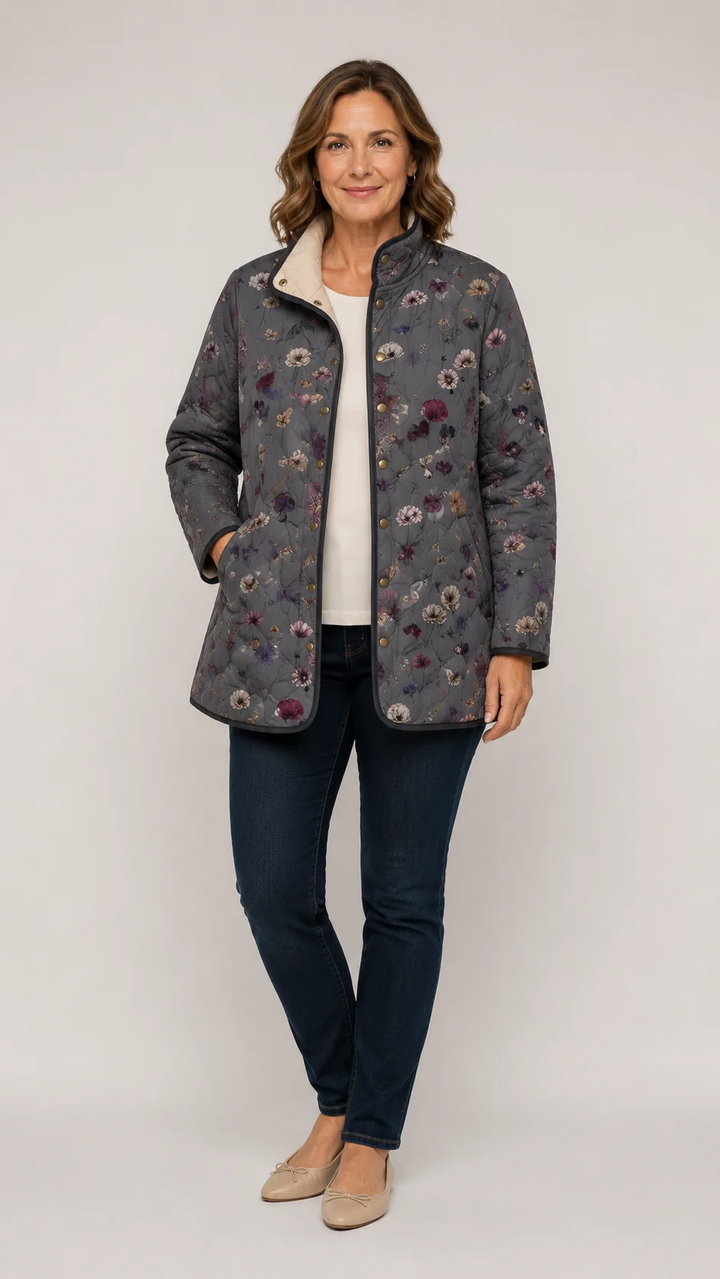 Woman wearing the grey quilted floral jacket open over a cream top, dark jeans and beige flats, one hand in a pocket. 1