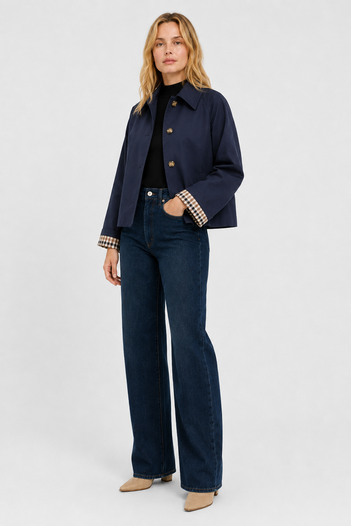 Women's navy blue lightweight jacket, another view with a hand in the pocket, worn with wide-leg jeans and beige boots.