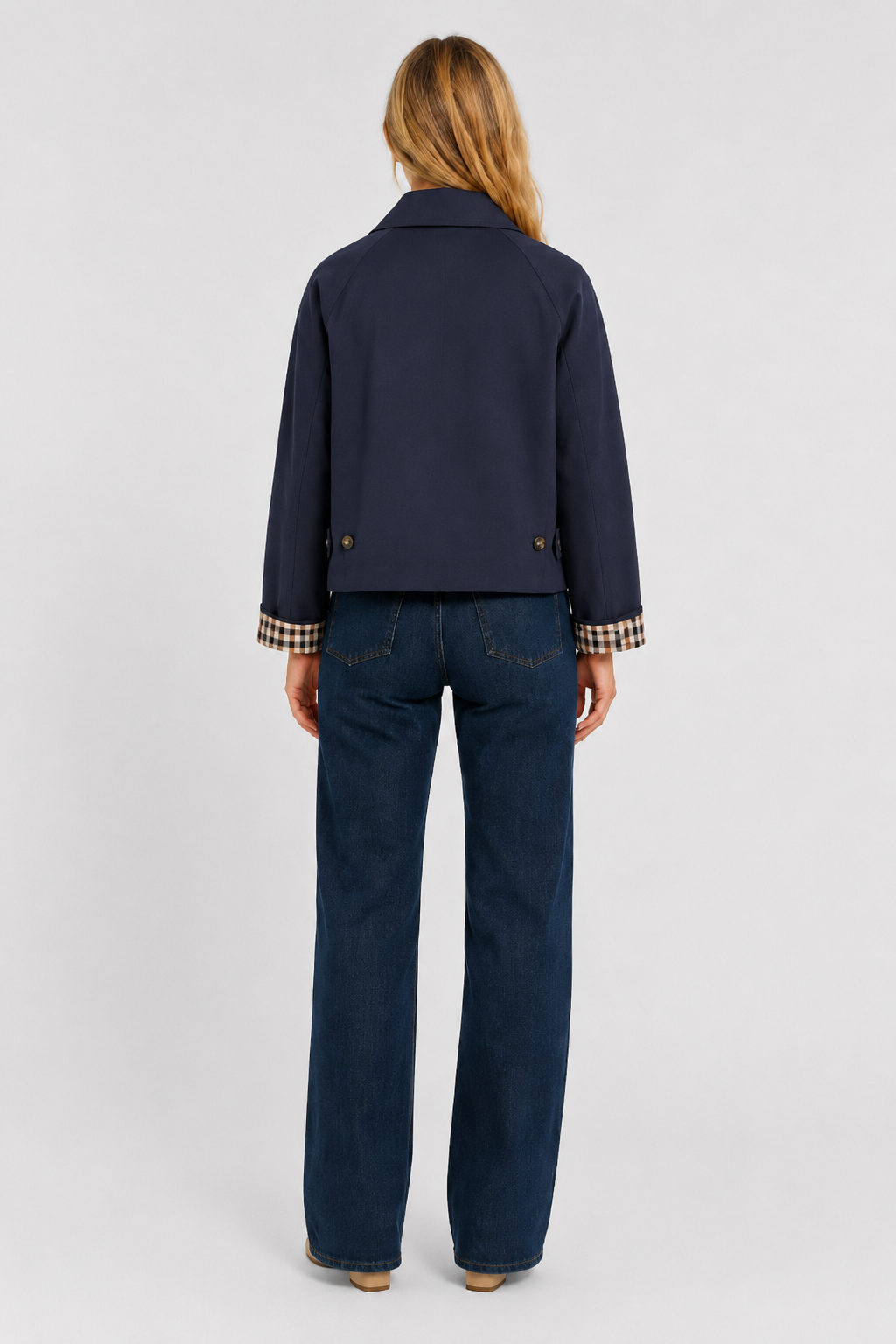 Women's navy blue lightweight jacket, back view with waist tabs and checked cuffs, worn with dark jeans.