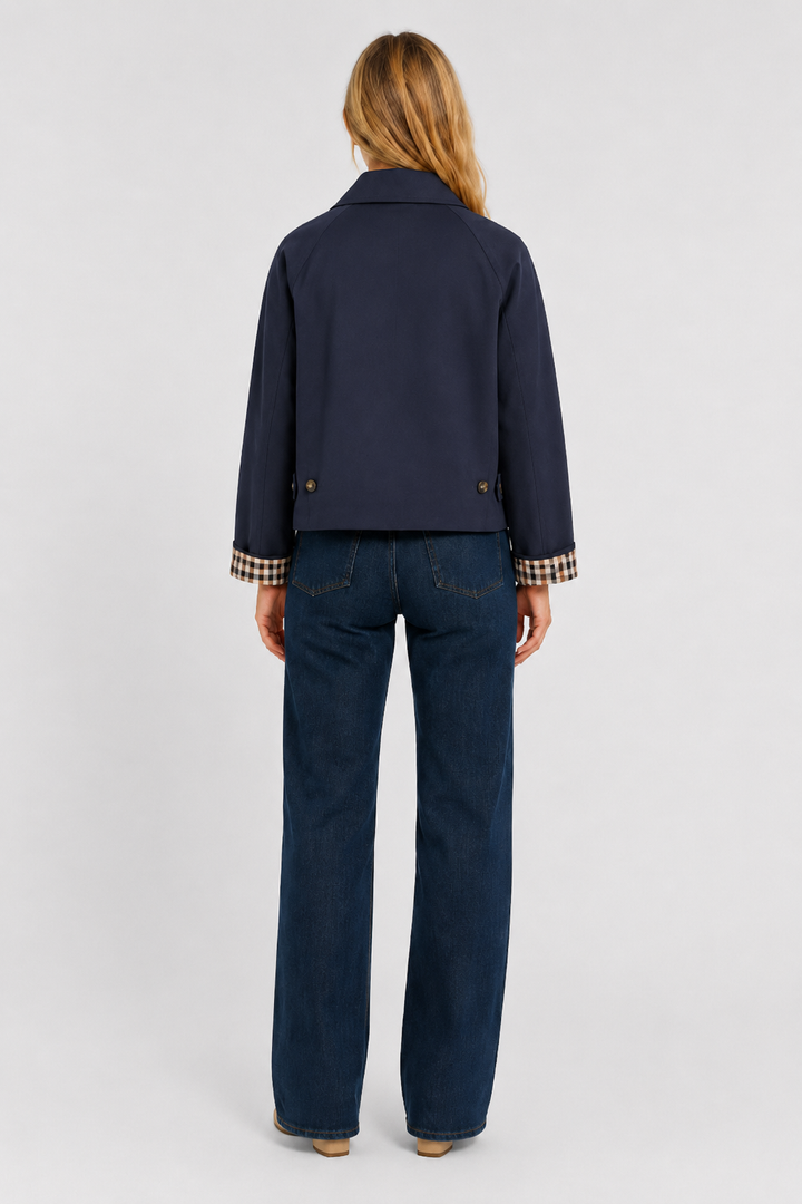 Women's navy blue lightweight jacket, back view with waist tabs and checked cuffs, worn with dark jeans.