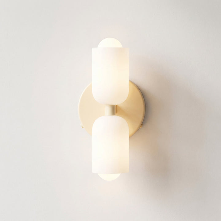 Front view of the wall light with a pale cream backplate and two frosted white glass shades, softly lit on a white wall. 10