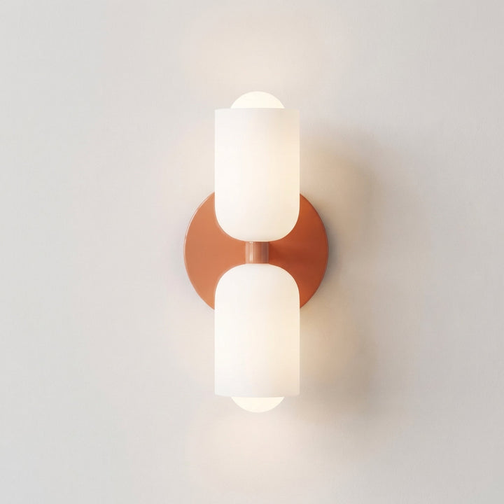 Front view of the wall light with a terracotta-orange round backplate and two frosted white glass shades, one up and one down. 9