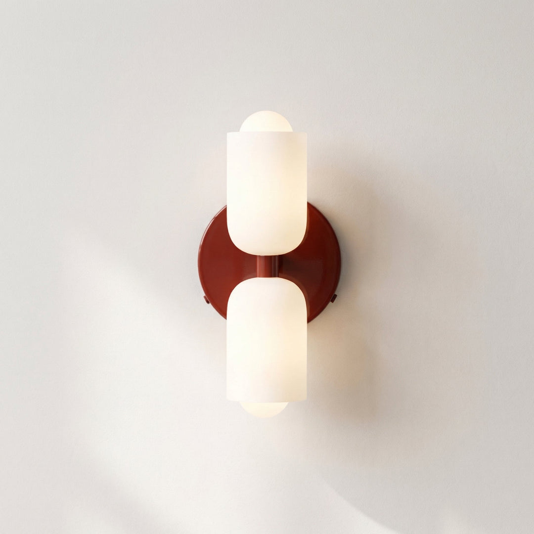 Front view of the wall light with a glossy burgundy-red backplate and two frosted white glass shades, lit against a pale wall. 13