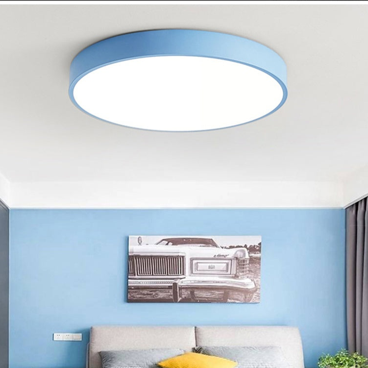 Light blue round flush-mount ceiling light without wood trim, glowing over a blue bedroom wall with a framed vintage car print.