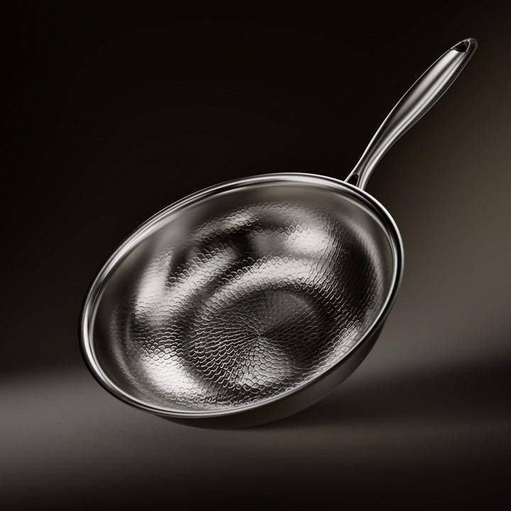 Wok pan tilted toward the camera, showing its hammered, scale-textured interior and long polished metal handle against a dark background. 1
