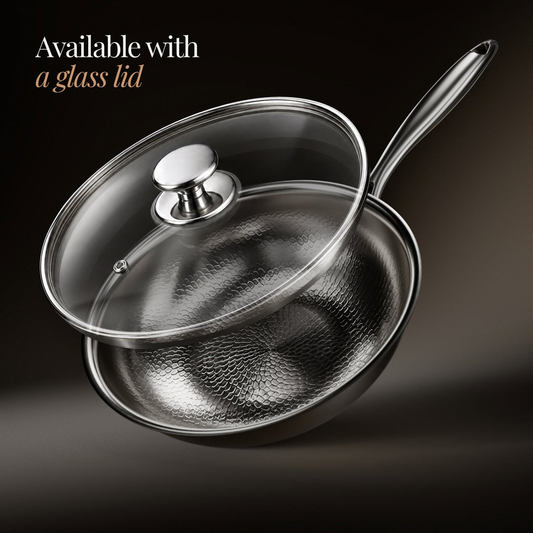 Hammered titanium wok pan with a clear glass lid and steel knob, detail.
