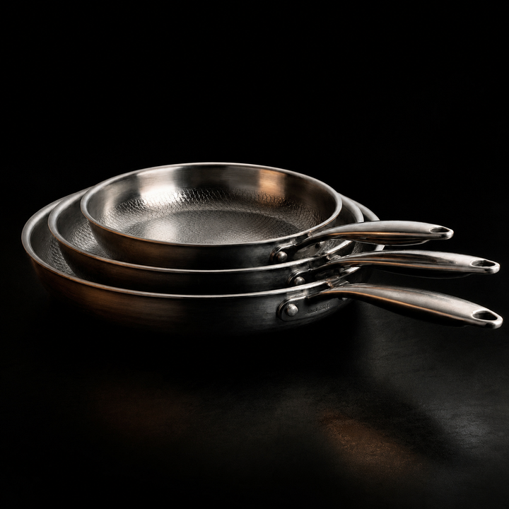 Three nested hammered-texture pans with handles fanned out to the right on a dark surface.