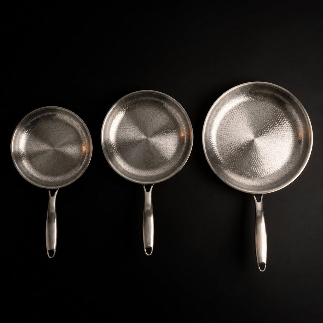 Top-down view of the three pans lined up in ascending size, each showing its hammered cooking surface and long handle.
