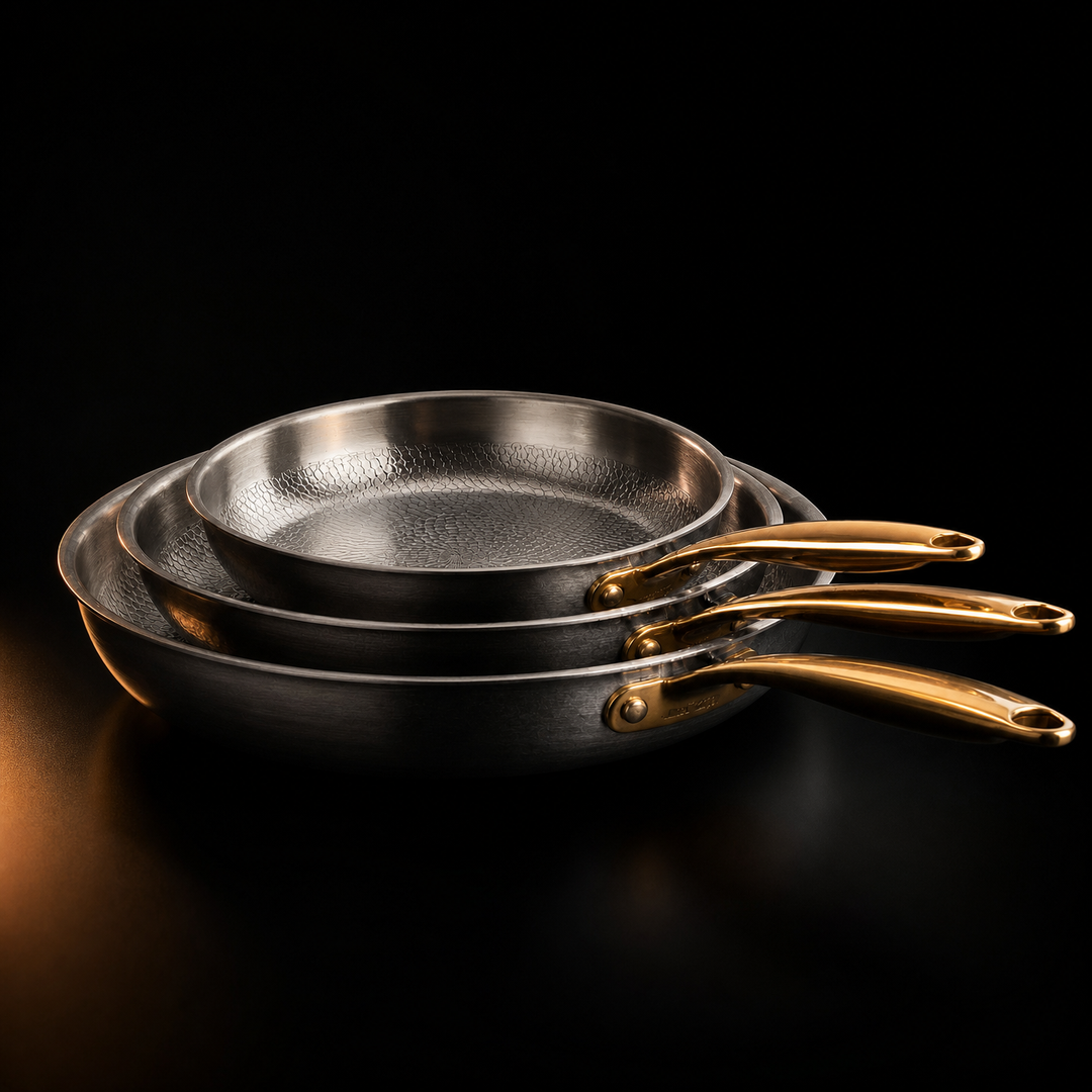 Three nested hammered-texture pans with gold-toned handles, staggered at a low side angle against a dark background.