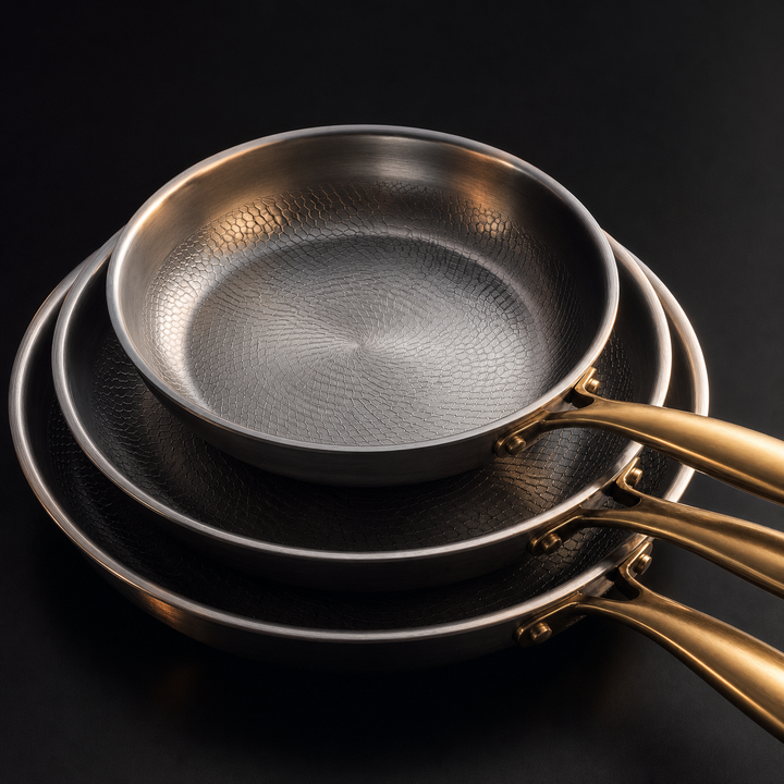Close-up detail of the stacked pans showing the textured cooking surface, rolled rims and riveted gold-toned handles.