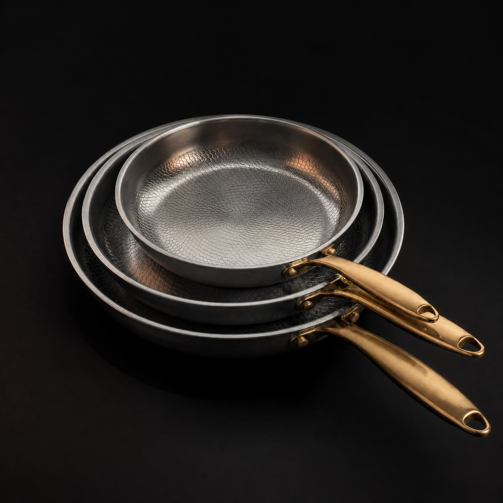 Three stacked pans detail showing the scale-like hammered pattern inside and the gold-toned handles.