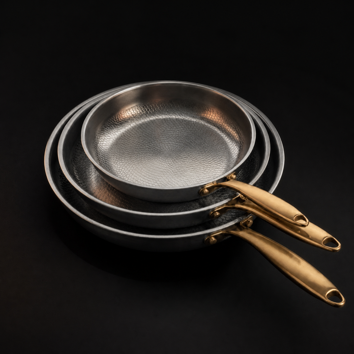 Three stacked pans detail showing the scale-like hammered pattern inside and the gold-toned handles.
