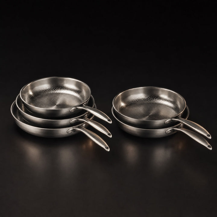 Detail of five silver hammered metal frying pans stacked together with sleek handles.