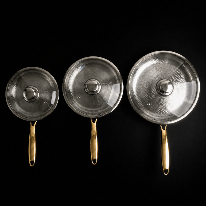 Top-down view of the three pans with glass lids on, each lid topped with a polished steel knob.