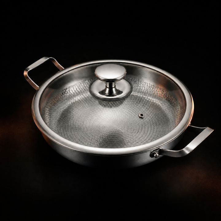 Pan with a clear glass lid and a polished metal knob on a black background, the hammered interior visible through the glass. 3