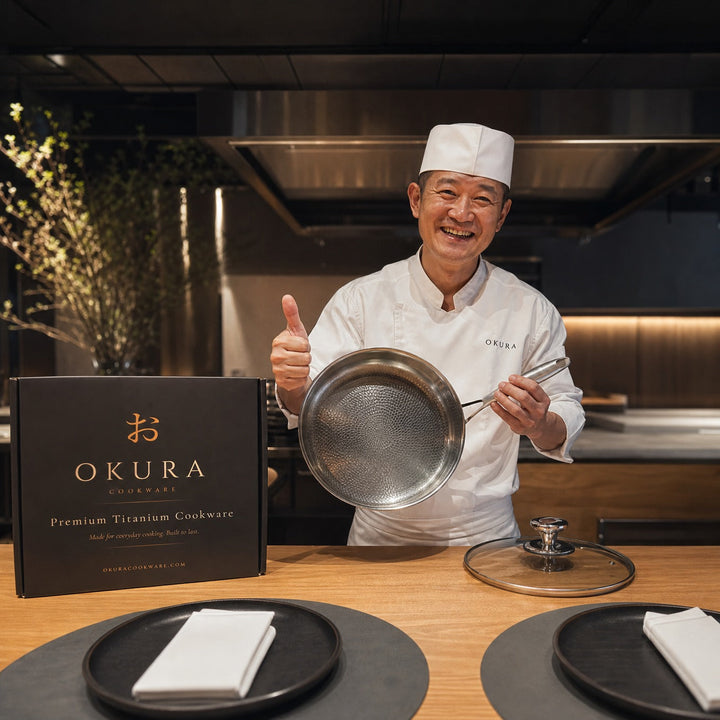 Smiling chef in whites giving a thumbs up while holding the pan, with the black box and glass lid on the counter.