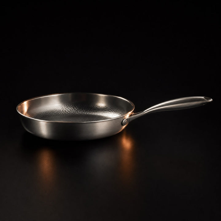 Single pan in side profile, showing its low brushed sidewall, riveted handle and warm reflections on the dark surface.