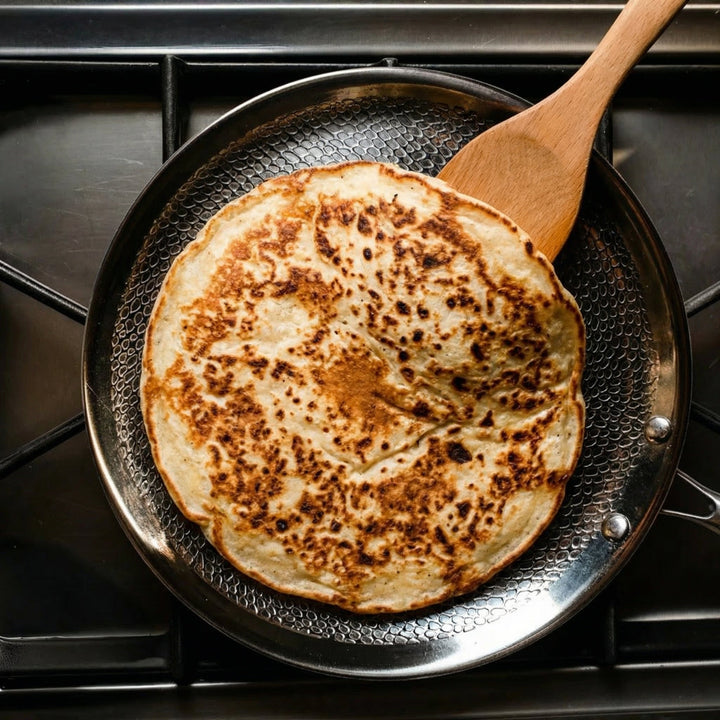 Hand-Hammered Titanium Crepe Pan, PFAS-Free with a crepe cooking in the pan on a gas stovetop.