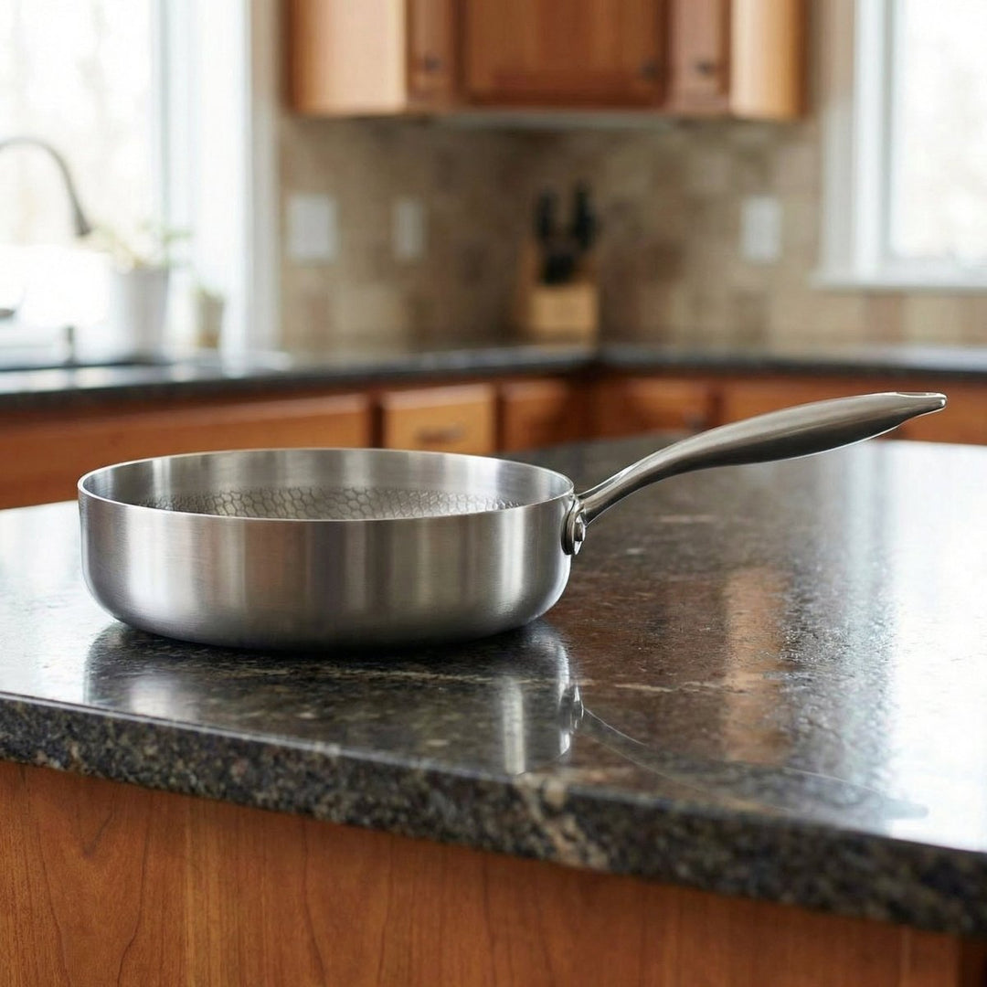 Another view of the silver Hand-Hammered High-Wall Titanium Frying Pan resting empty on a dark countertop.