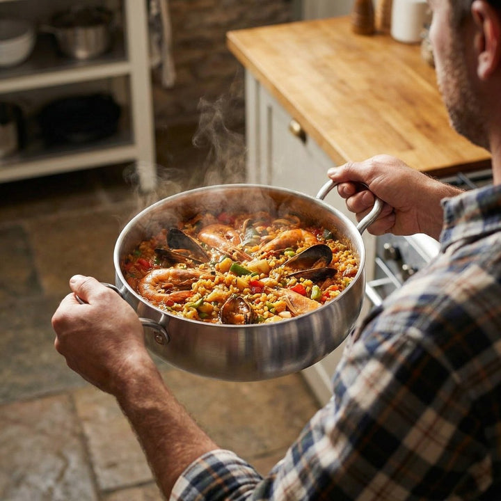 Another view of a man holding the stockpot filled with steaming seafood paella in a kitchen.