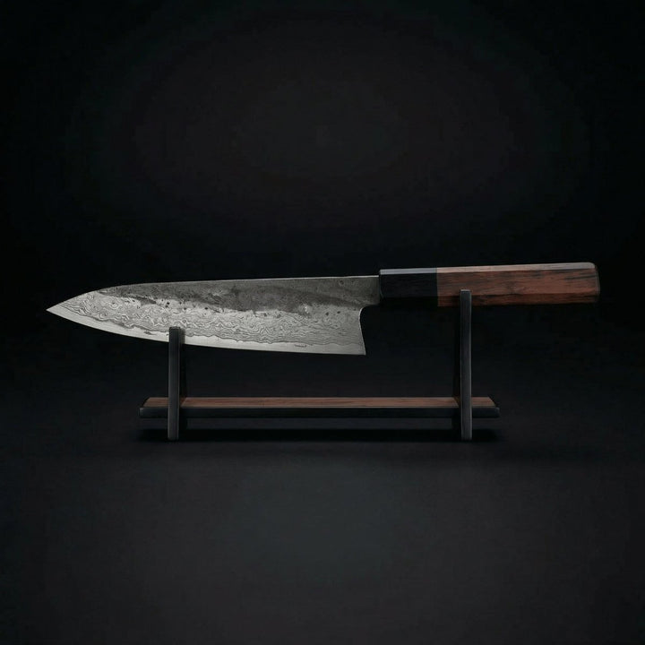 Kiritsuke knife detail on a wooden and black metal display stand against a dark background.