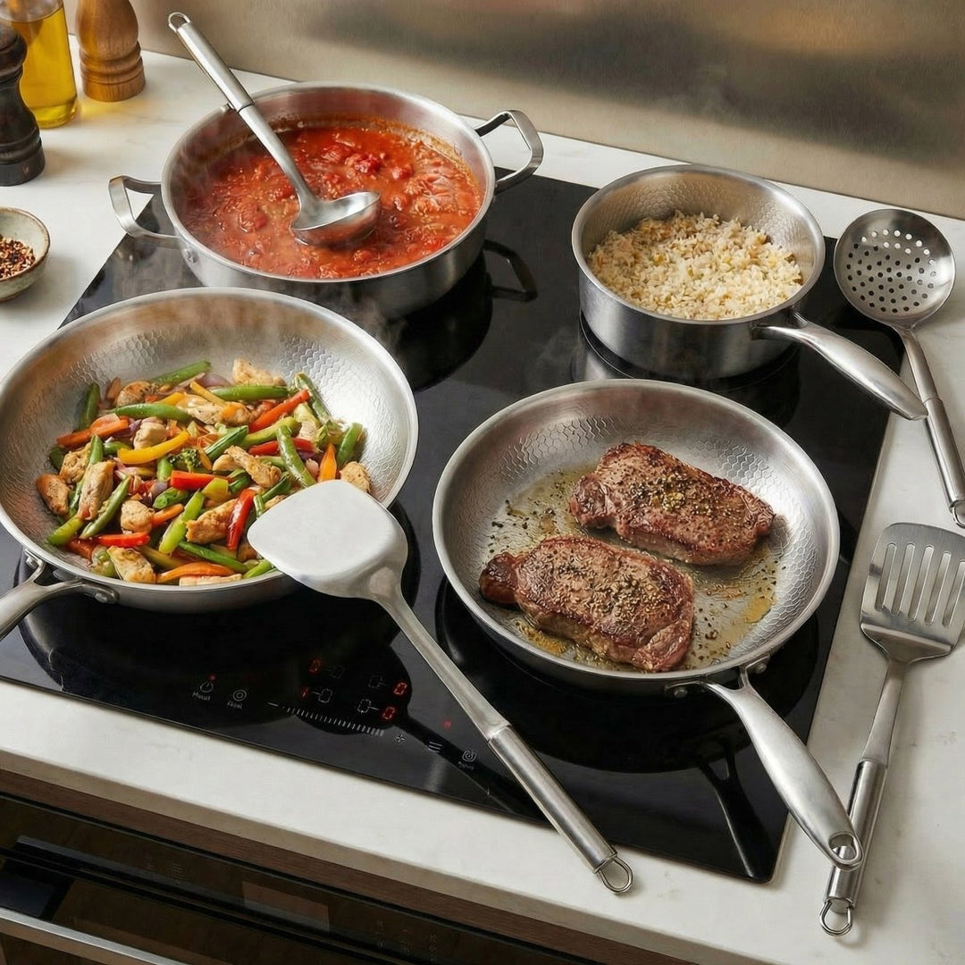 Pans on an induction cooktop with vegetables, seared steaks, rice and tomato sauce, with utensils nearby.