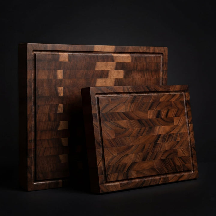 Two walnut end-grain boards of different sizes leaning together against a dark backdrop, their grooved surfaces facing the camera. 3