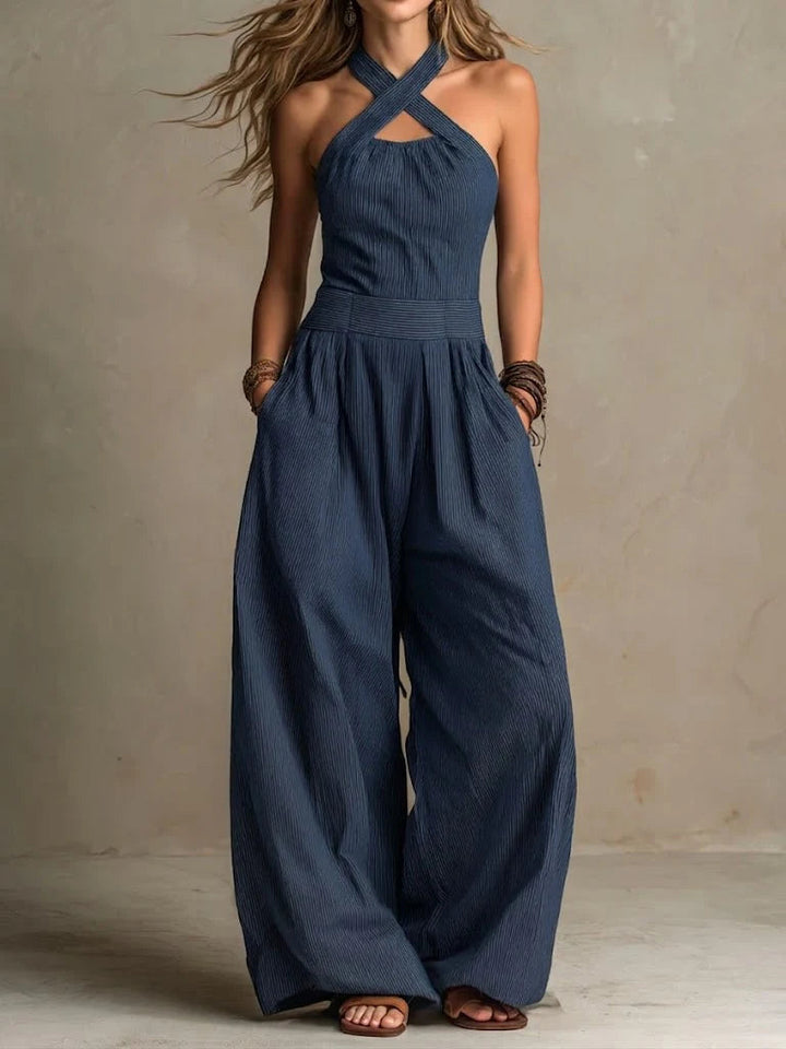 Same crossed-strap halter jumpsuit in navy blue pinstripe, worn with stacked bracelets and flat sandals 3