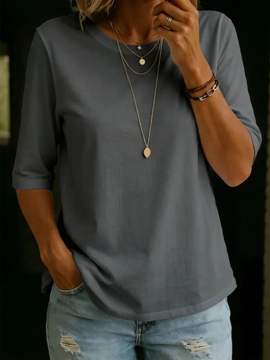 Woman wearing a slate gray half-sleeve crew-neck tee with layered gold necklaces, stacked bracelets and ripped light-wash jeans. 7