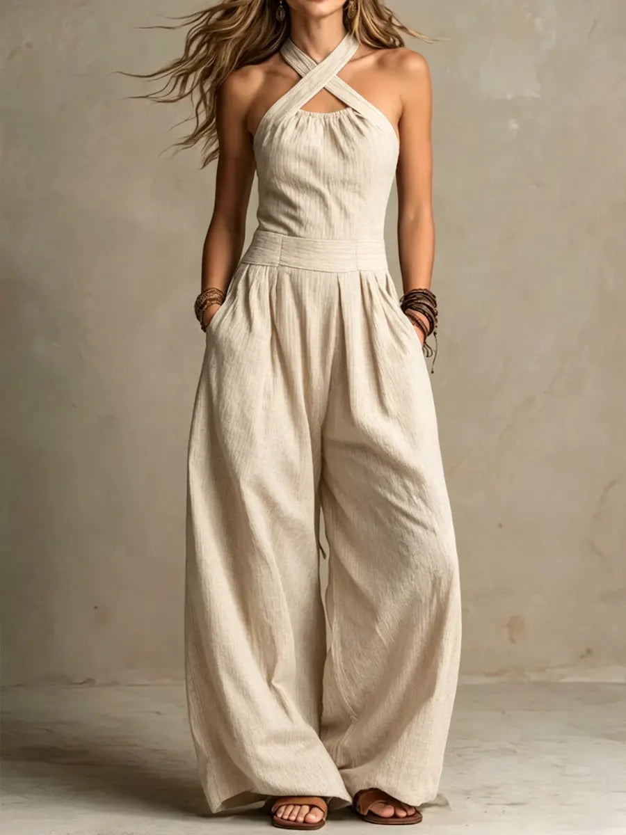 Same crossed-strap halter jumpsuit in a light beige textured fabric, worn with wide legs and brown sandals 2