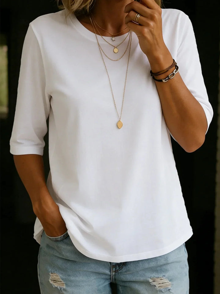 Woman wearing a white half-sleeve crew-neck tee with layered gold necklaces, a leather bracelet and ripped light-wash jeans. 1