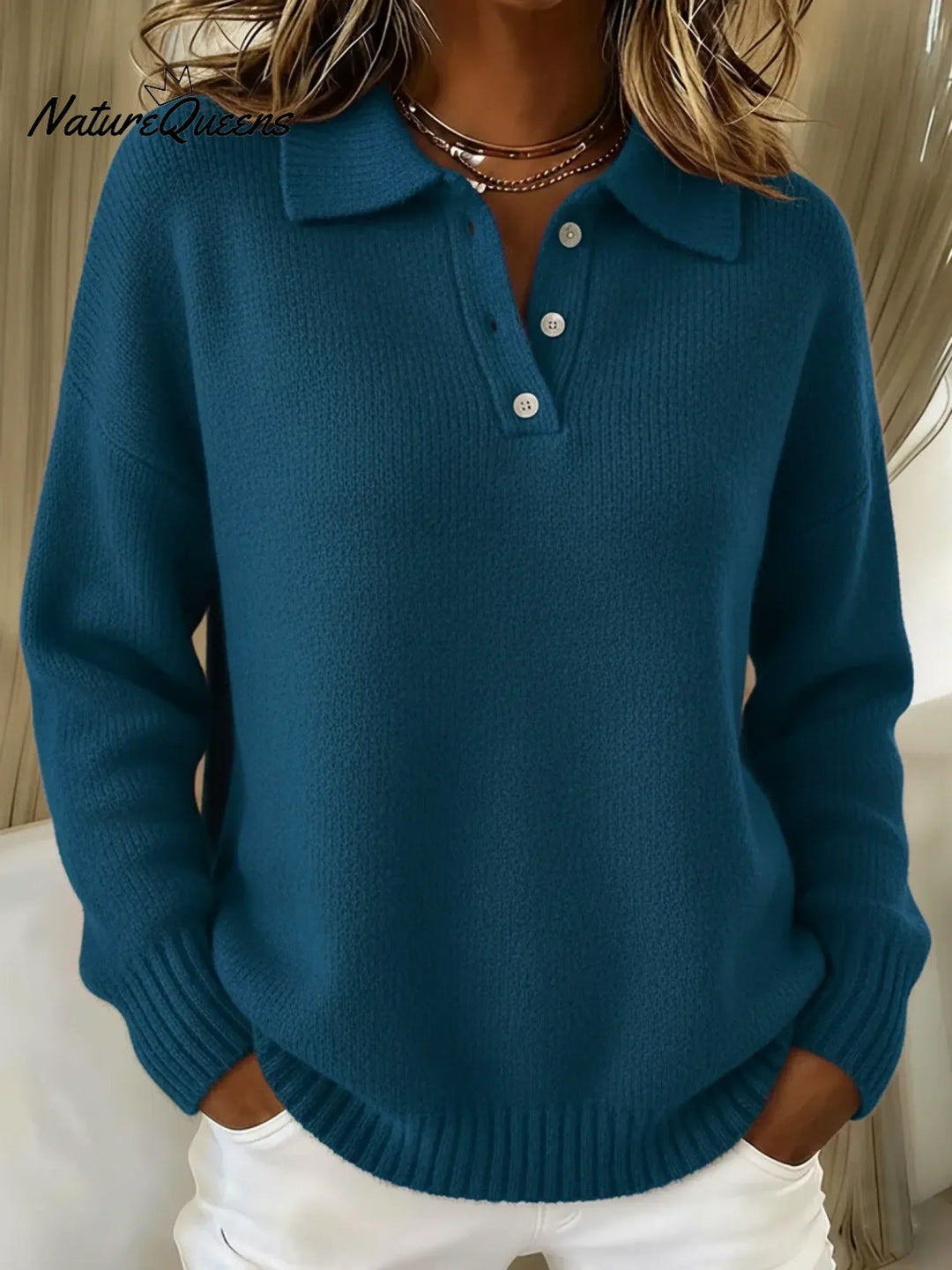 Deep teal blue polo sweater with a folded collar and buttoned placket, styled with white pants.