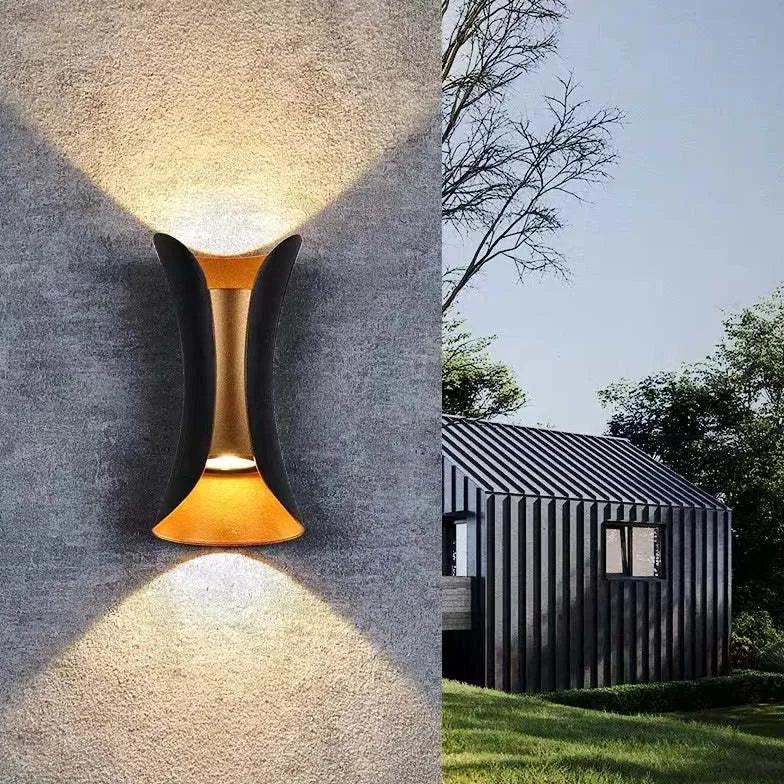 Black LED outdoor wall light with gold accents on a gray textured wall.