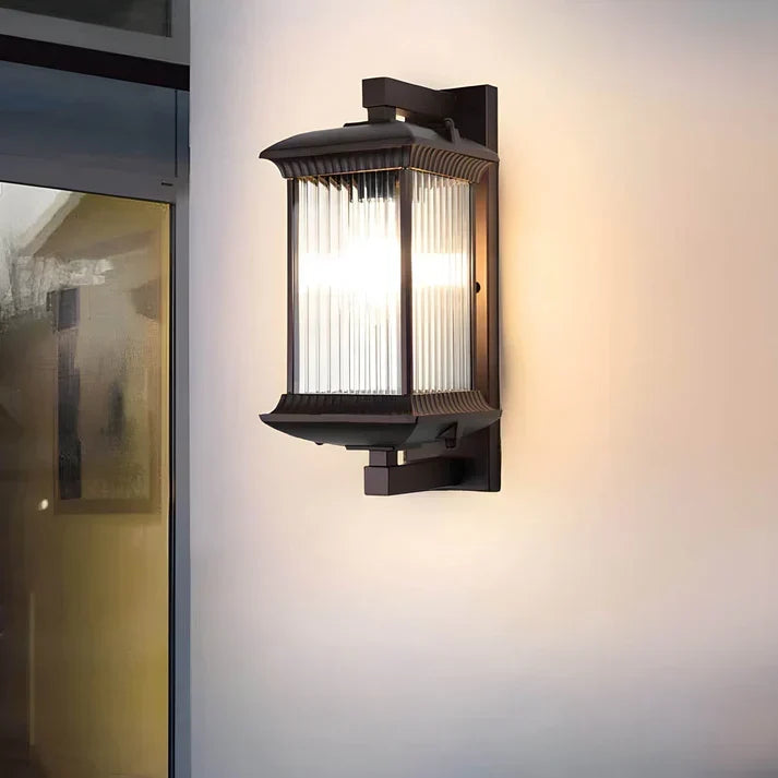 Lantern wall light with ribbed glass panels glowing on a pale wall next to a glass door. 3