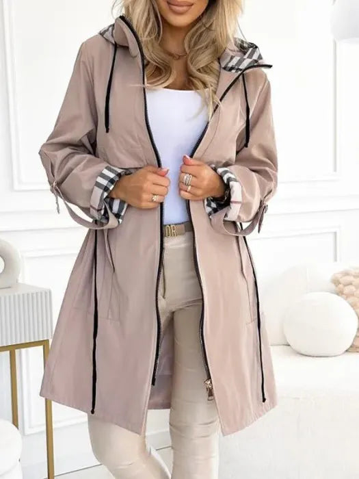 Woman in the light beige hooded jacket, worn open over a white top and beige pants, with drawstring hood and plaid cuff lining.