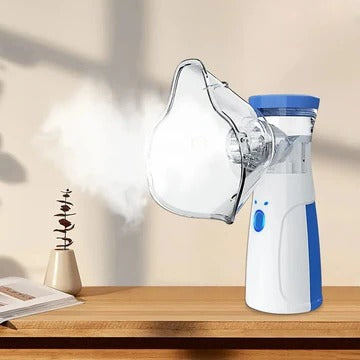 Blue and white handheld nebulizer with clear face mask on a wooden shelf beside a plant and open book.