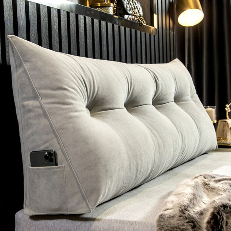 Grey velvet wedge pillow with tufted buttons and a side pocket holding a phone.